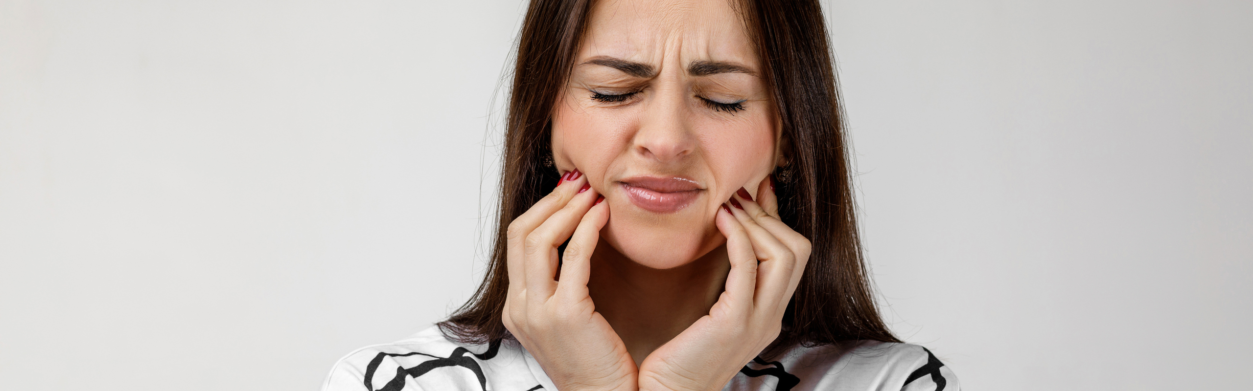 Kvinna med tandvärk som håller om käkarna och grimaserar.