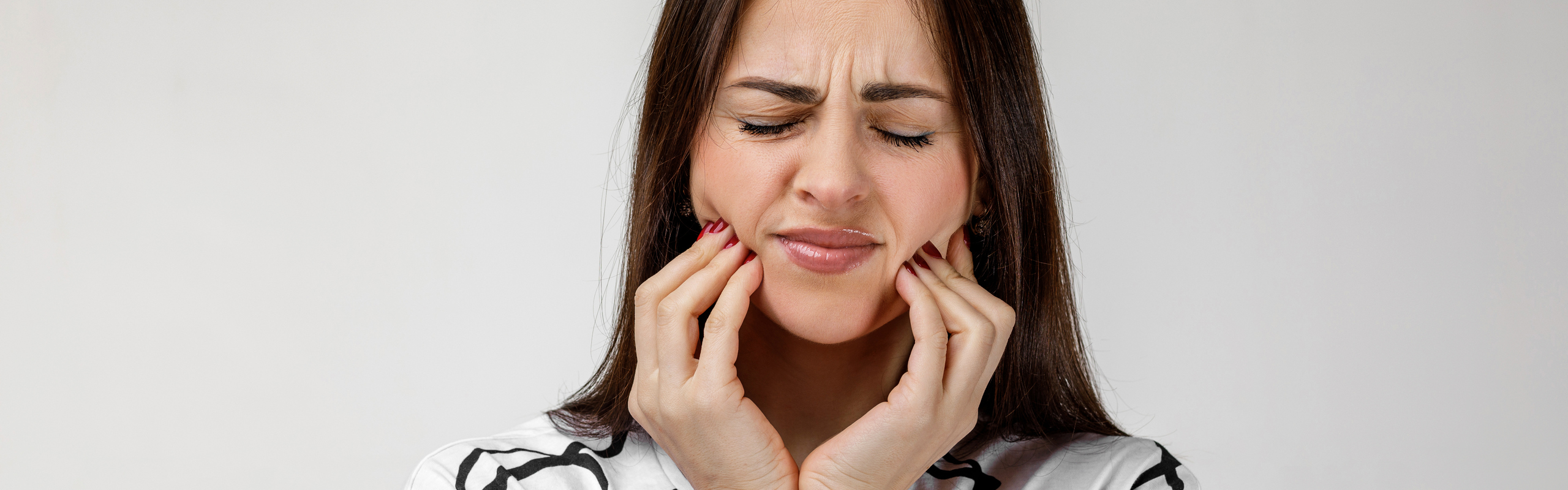 Kvinna med tandvärk som håller om käkarna och grimaserar.