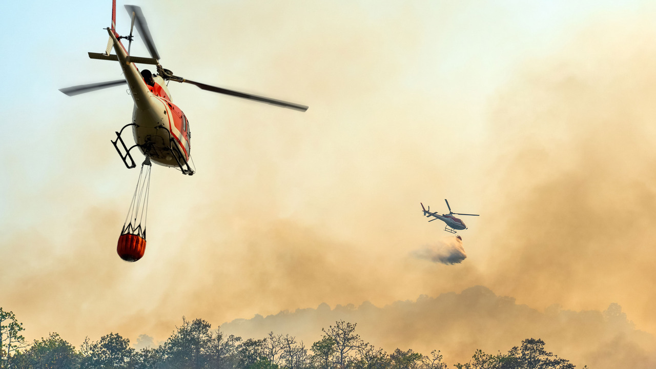 Två brandsläckningshelikoptrar dumpar vatten på en skogsbrand