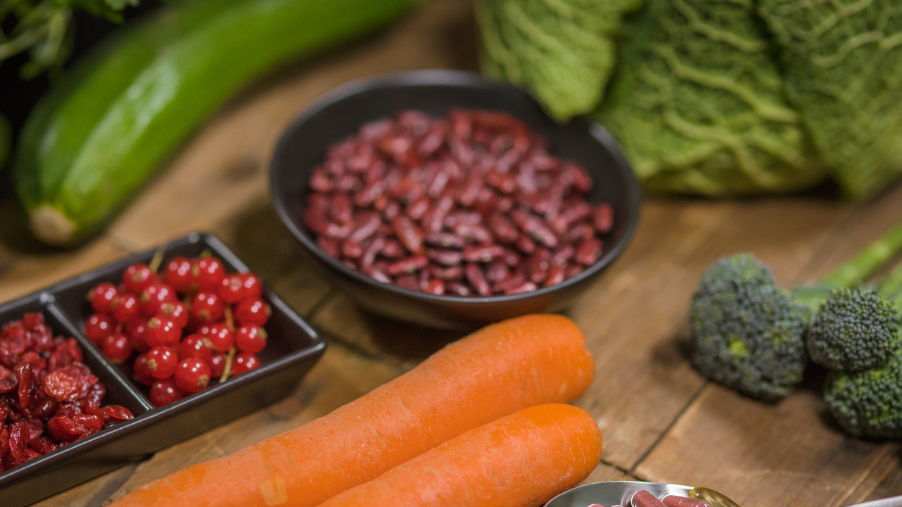 Nyttiga råvaror på ett bord och kosttillskott i pillerform i en sked bredvid.