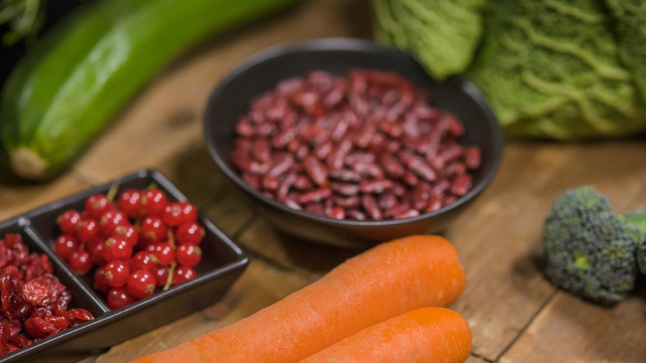 Nyttiga råvaror på ett bord och kosttillskott i pillerform i en sked bredvid.