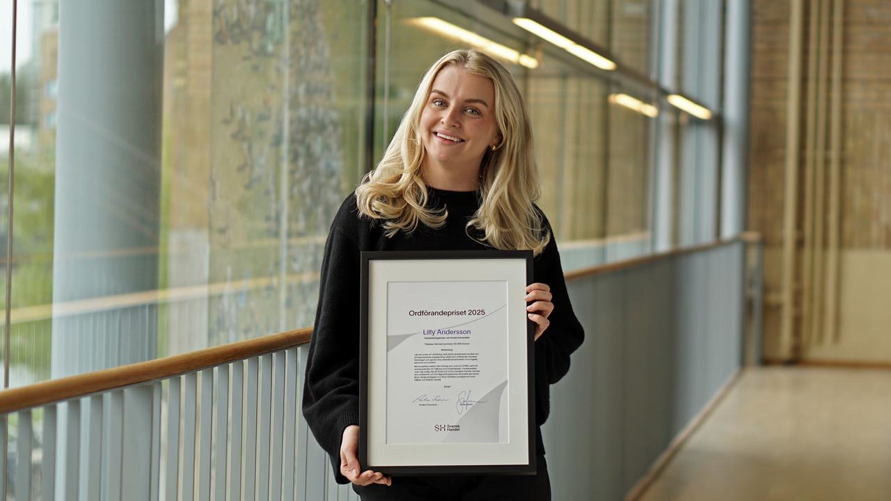 En kvinna håller i ett inramat dokument i en korridor.