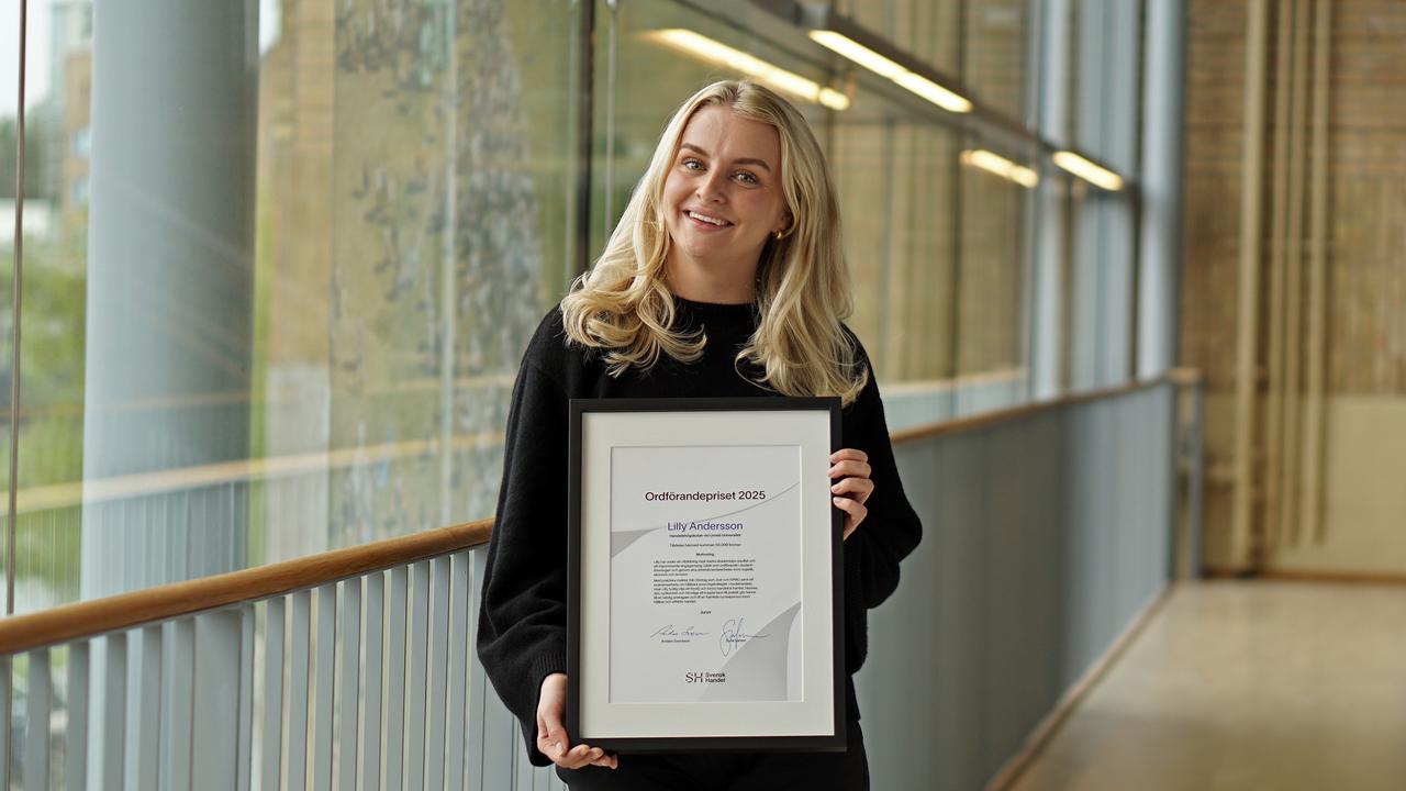 En kvinna håller i ett inramat dokument i en korridor.