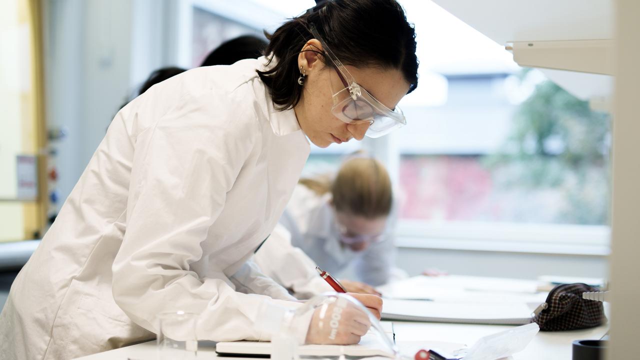 Bild på student som lutar sig över en bänk och skriver i en labbrapport.