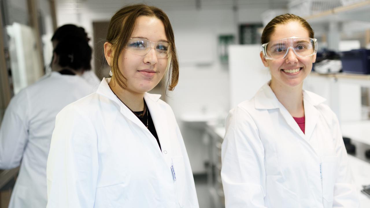 Bild på två studenter i vita labbrockar stående i ett kemilaboratorium.