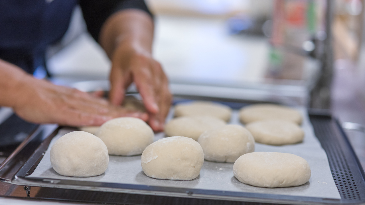 Händer som formar degklumpar till bröd på en plåt.