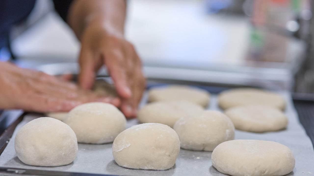 Händer som formar degklumpar till bröd på en plåt.