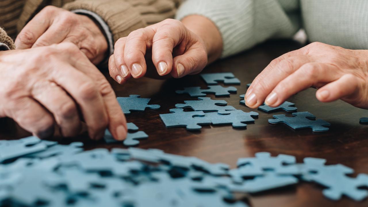 Två äldre personer lägger pussel tillsammans. Närbild på händer.