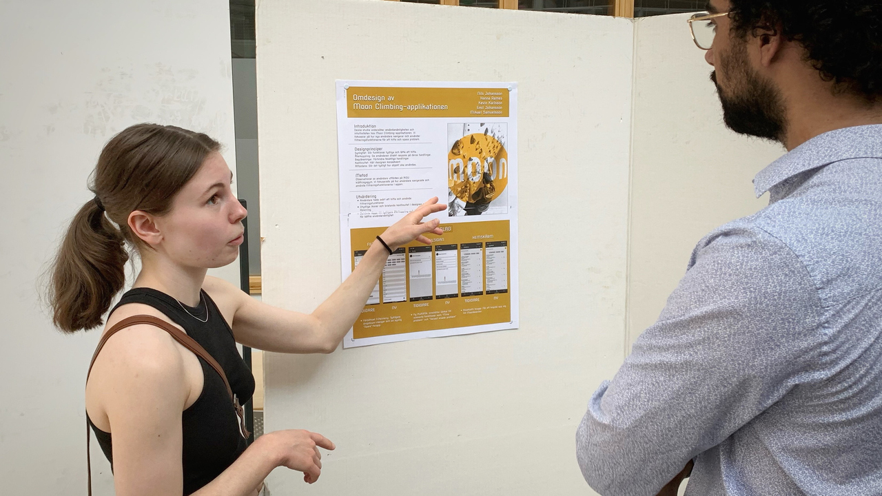 Hanna Remes, student på civilingenjörsprogrammet i teknisk datavetenskap, pekar och förklarar sin lösning inom interaktionsteknik, för amanuens Ahmad Kalash, som lyssnar.