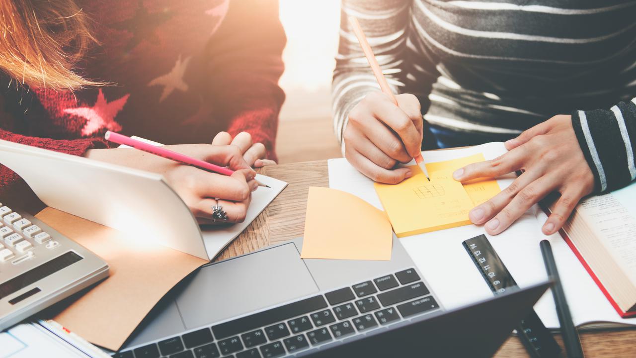 Två personer som sitter med datorer och block och skriver. Grupparbete.