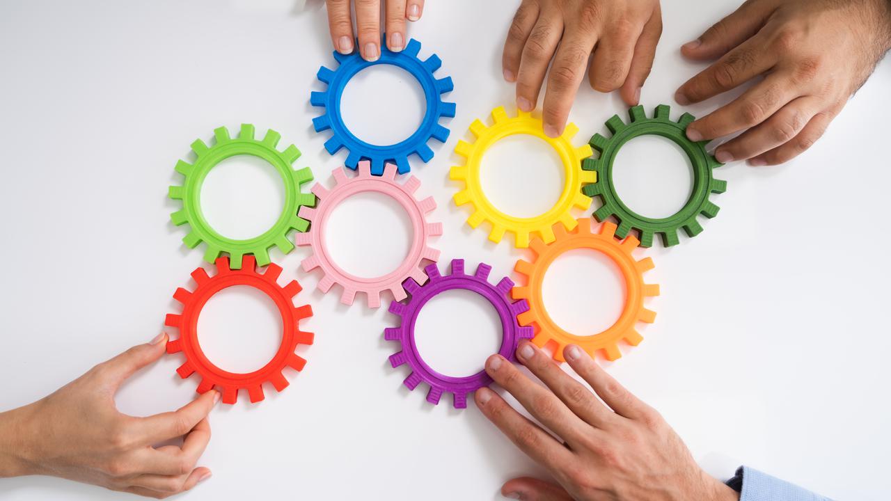 Händer som fogar ihop färgglada plastkugghjul.