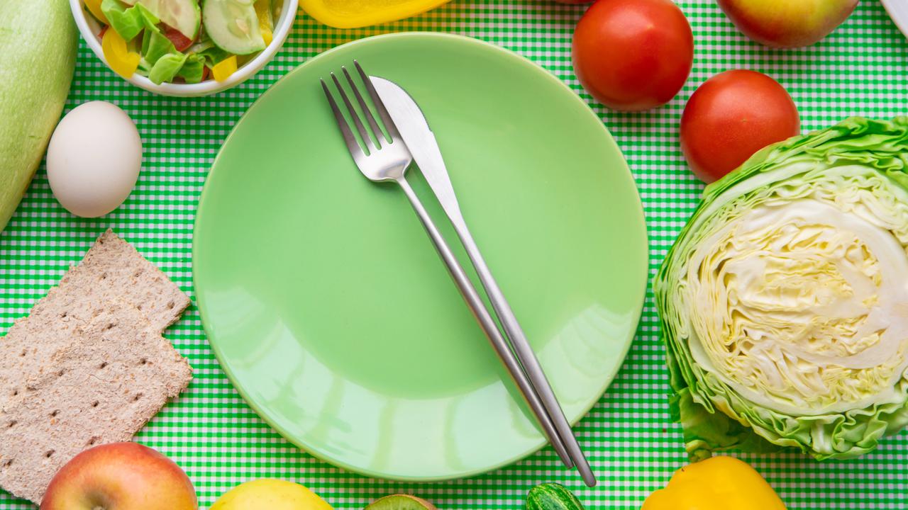 Tallrik och bestick omringad av nyttiga livsmedel såsom frukt och grönsaker.
