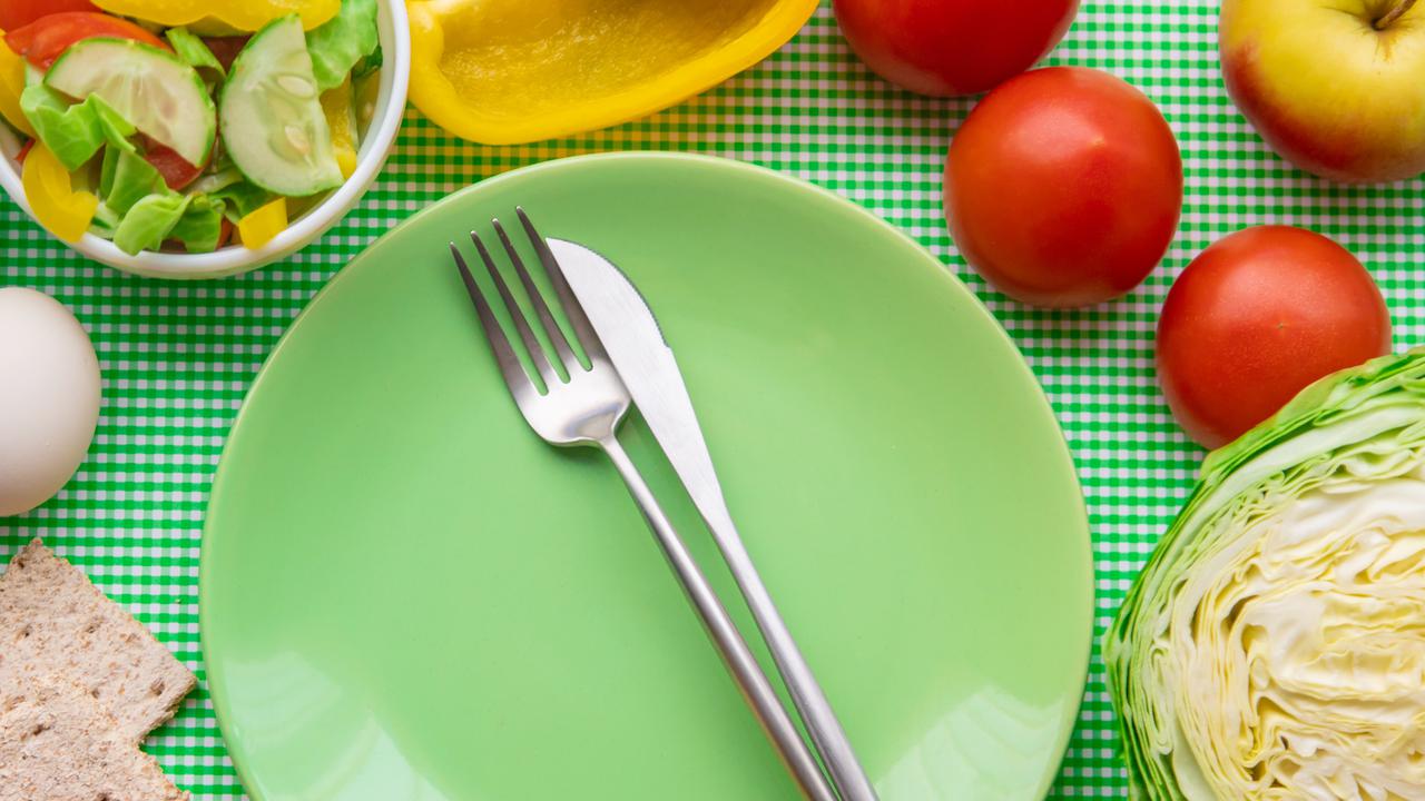 Tallrik och bestick omringad av nyttiga livsmedel såsom frukt och grönsaker.