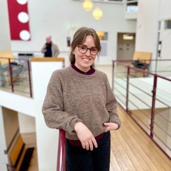 Kvinna står lutad mot ett räcke med en ljusgård i bakgrunden.