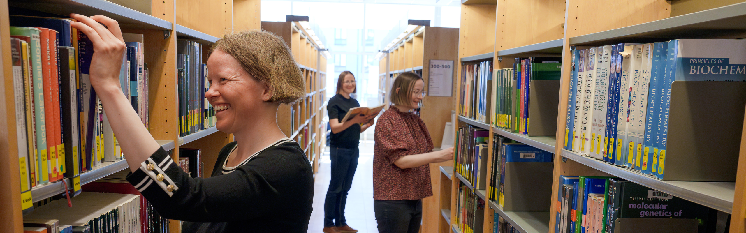 Tre systrar står mellan bokhyllor