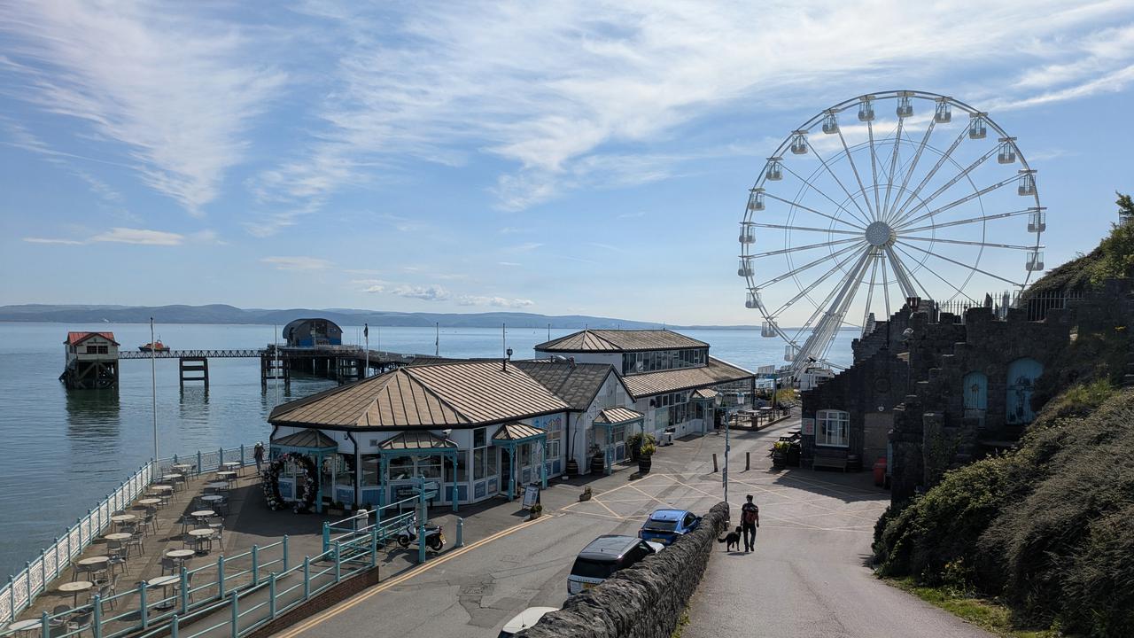 Pir med pariserhjul och byggnad längs strandkanten.