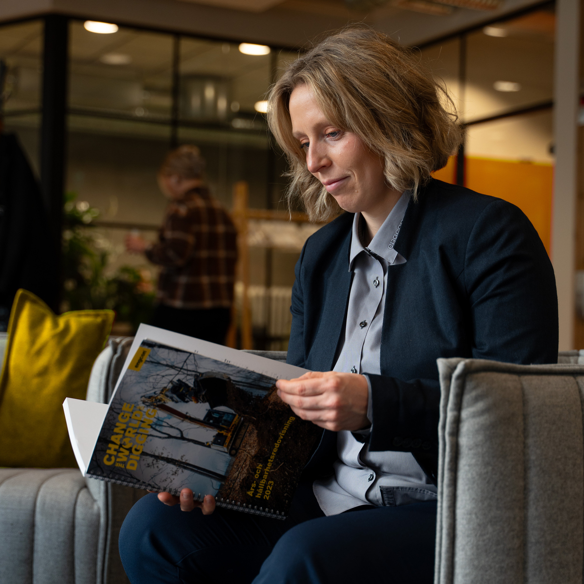 En kvinna sitter i en soffa och läser en tidning.