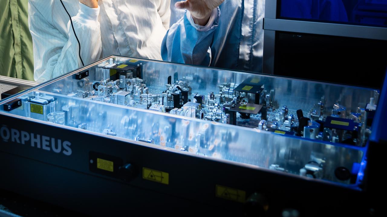 Två män i skyddskläder tittar på laserutrustning.