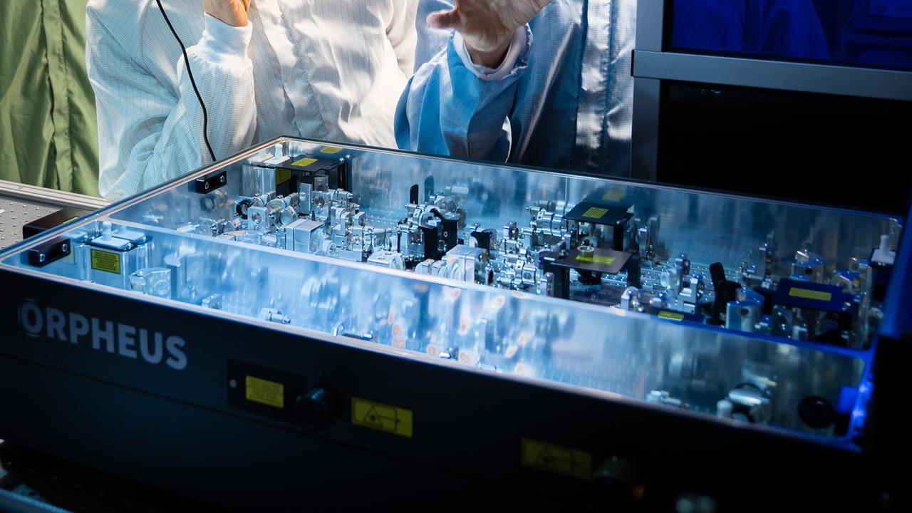 Två män i skyddskläder tittar på laserutrustning.