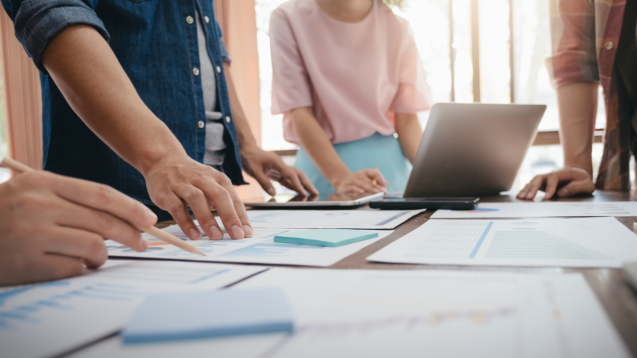 Personer som samarbetar. Detalj med händer, dator, papper på ett bord.