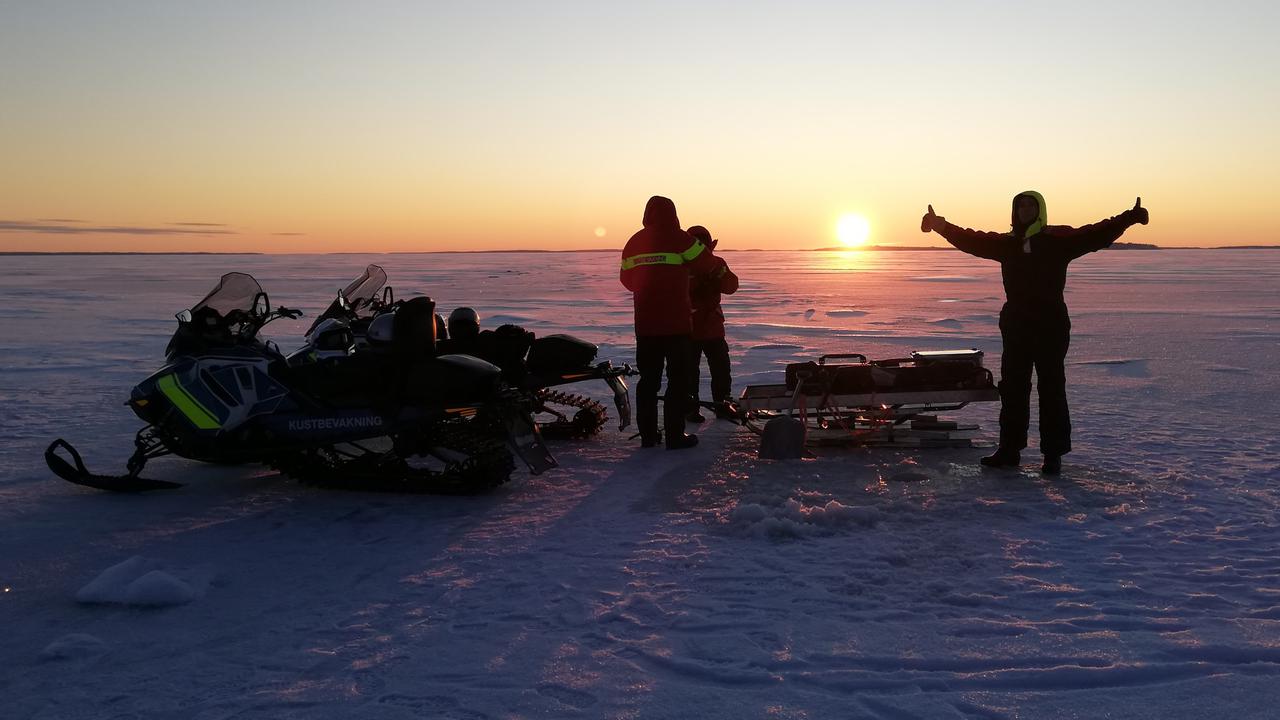 Tre personer står på havsis med skotrar och provtagningsutrustning medan solen knappt når över horisonten