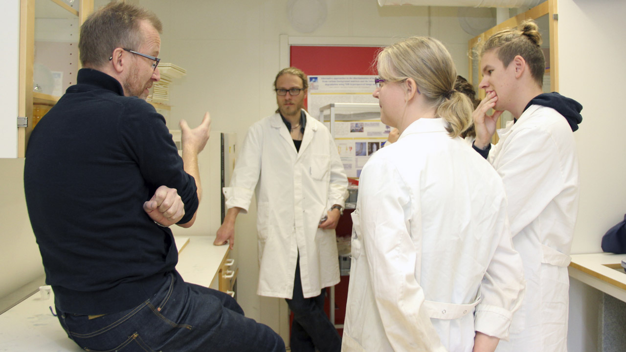 A teatcher instructing a group of students about to analyze soil samples from a stone age hut