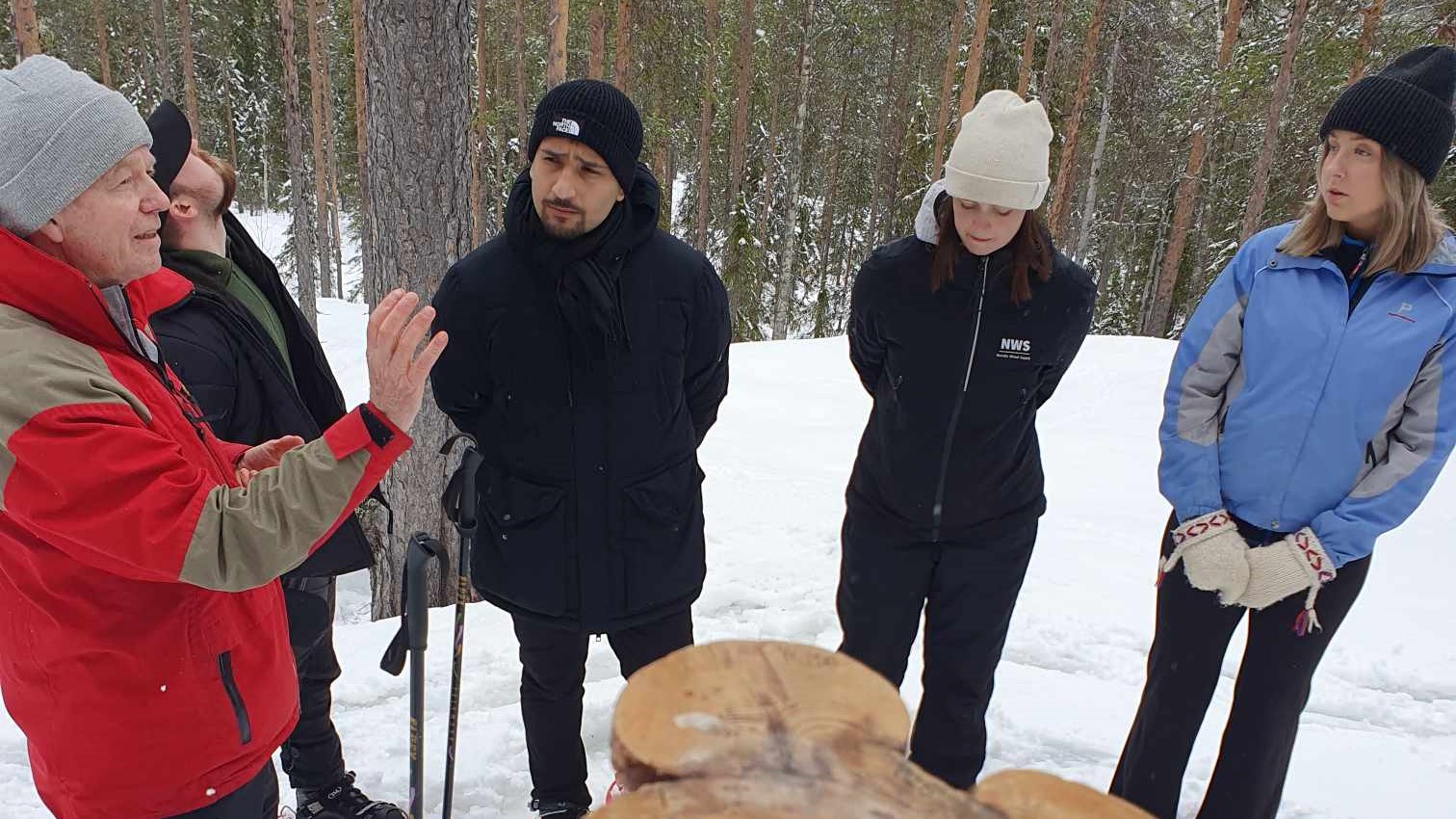 Fem personer står runt en stor stubbe i skogen