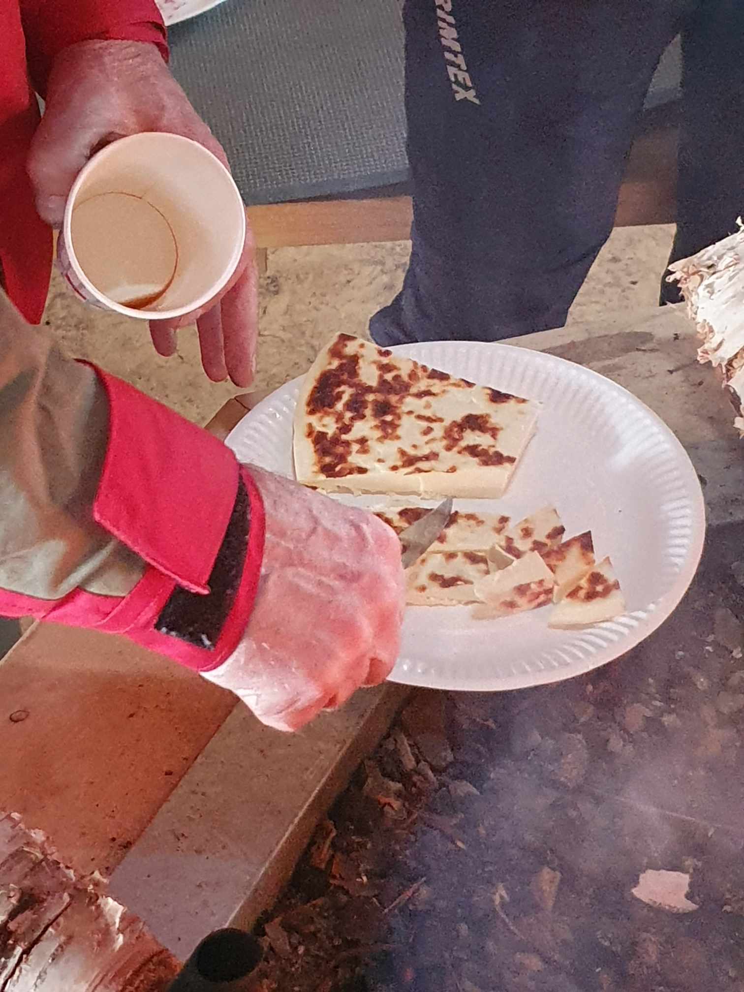 Närbild på en hand som skär upp kaffeost  på en papperstallrik.