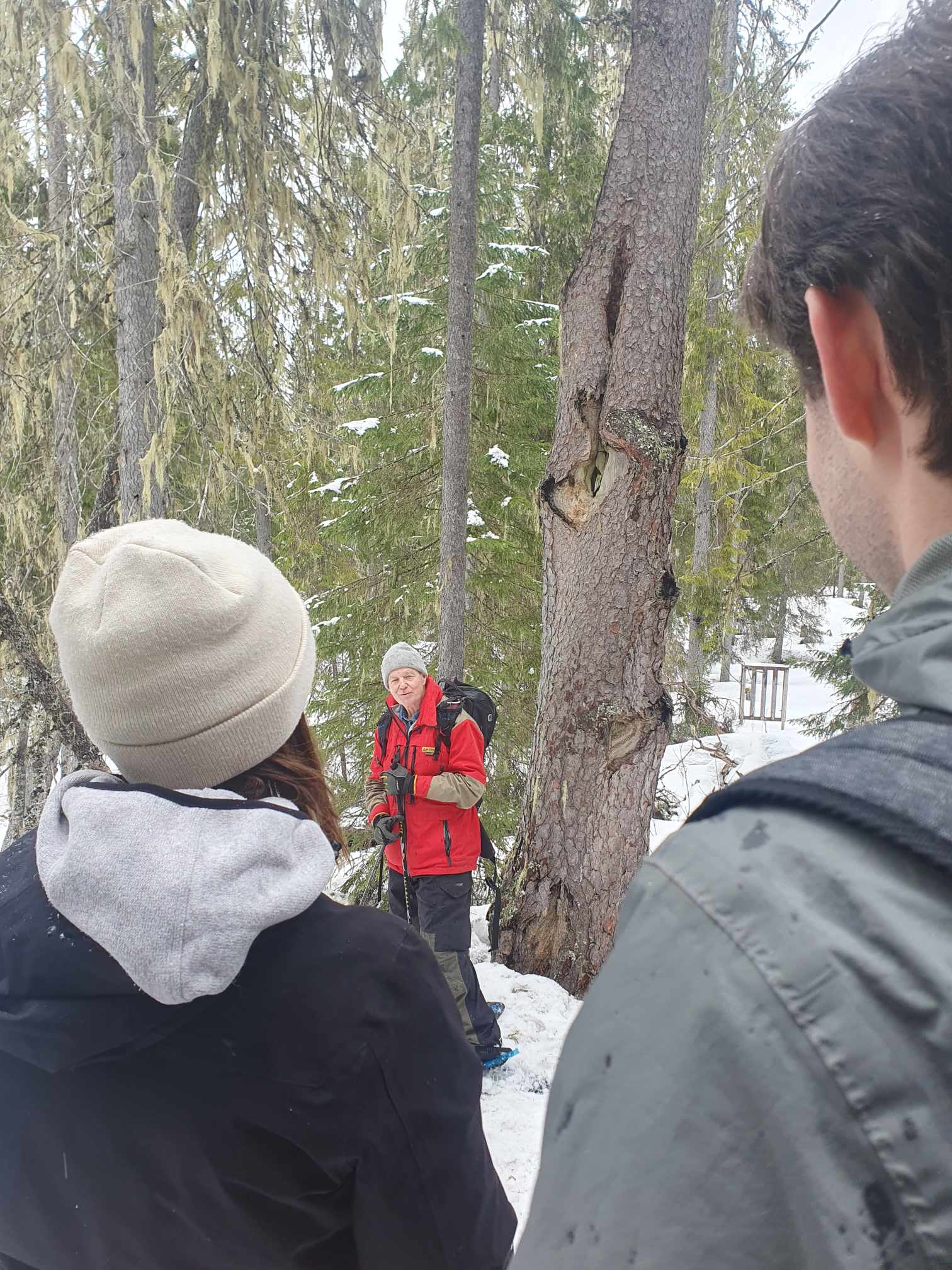En man står vid ett stort träd och berättar. Två lyssnande personer i förgrunden.