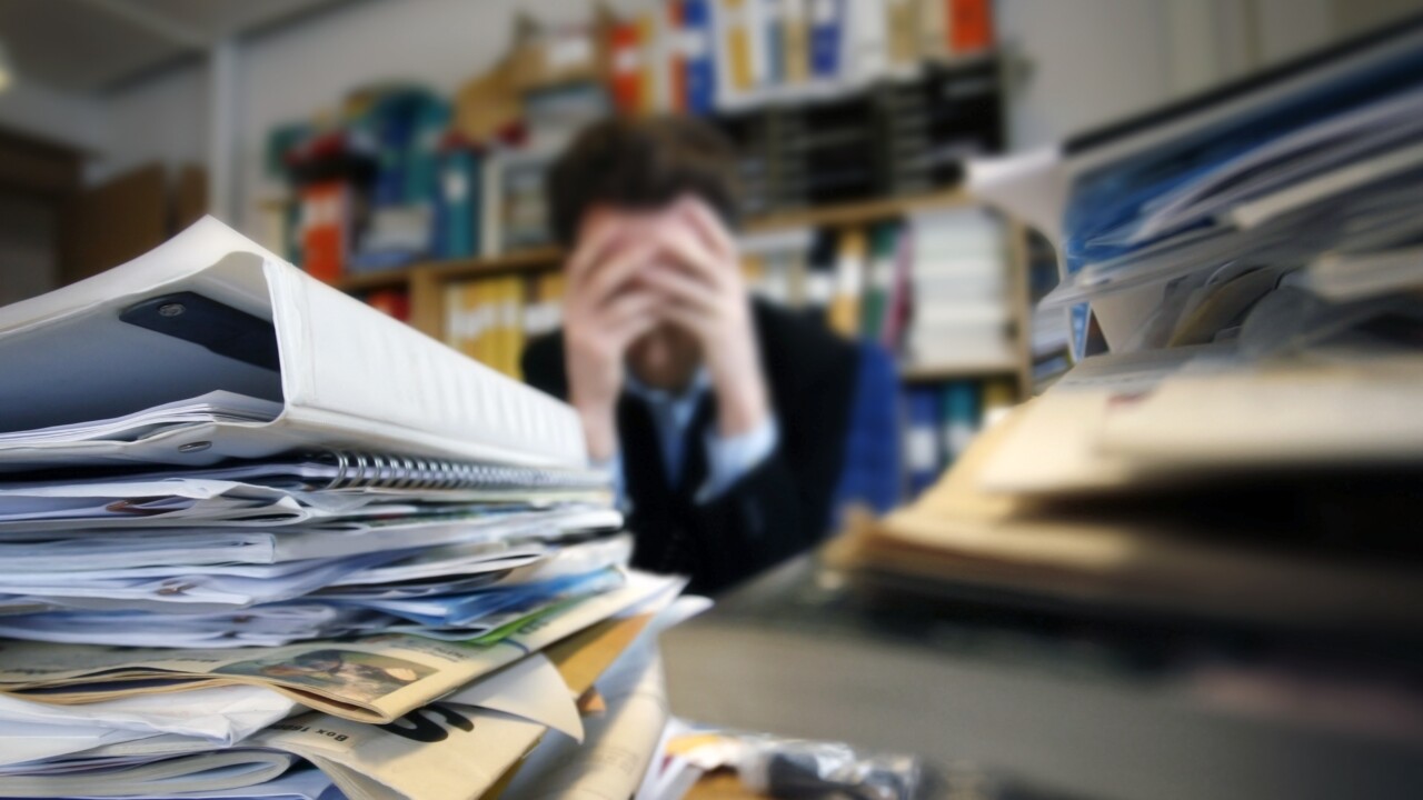 Person sitter frustrerad bland högar med papper