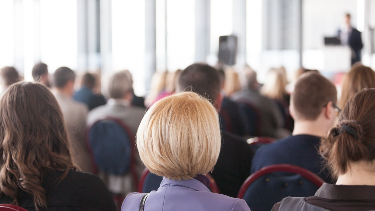 A large audience sitting in fron of a male speaker at a podium