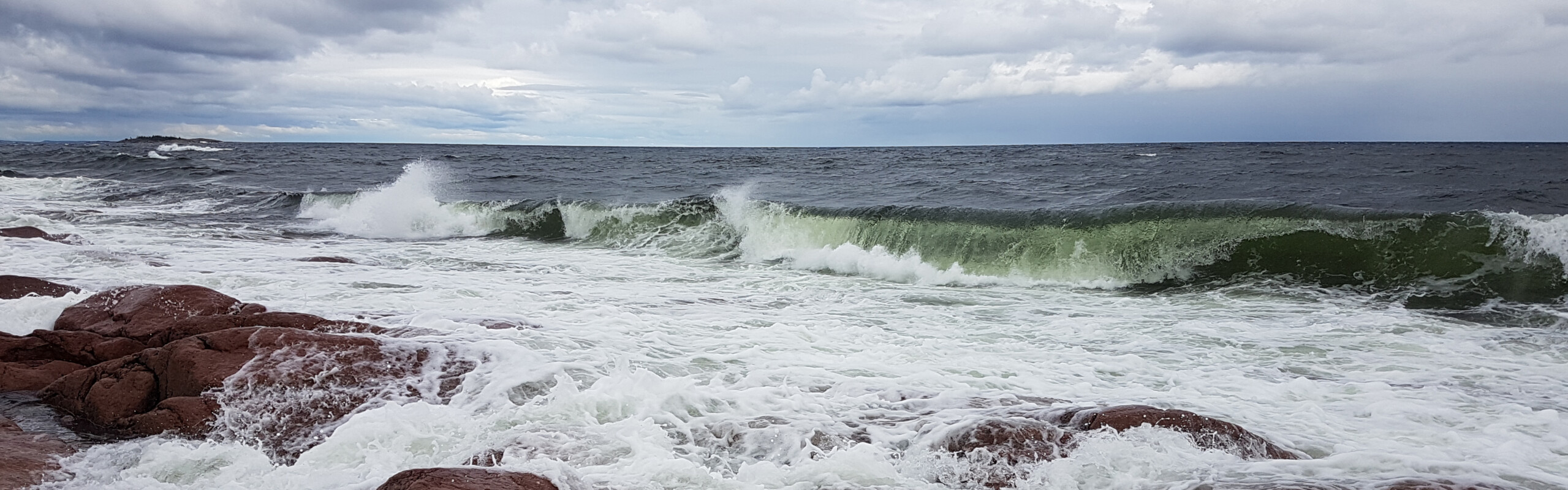 vågor slår mot röda klippor och en dramatisk himmel