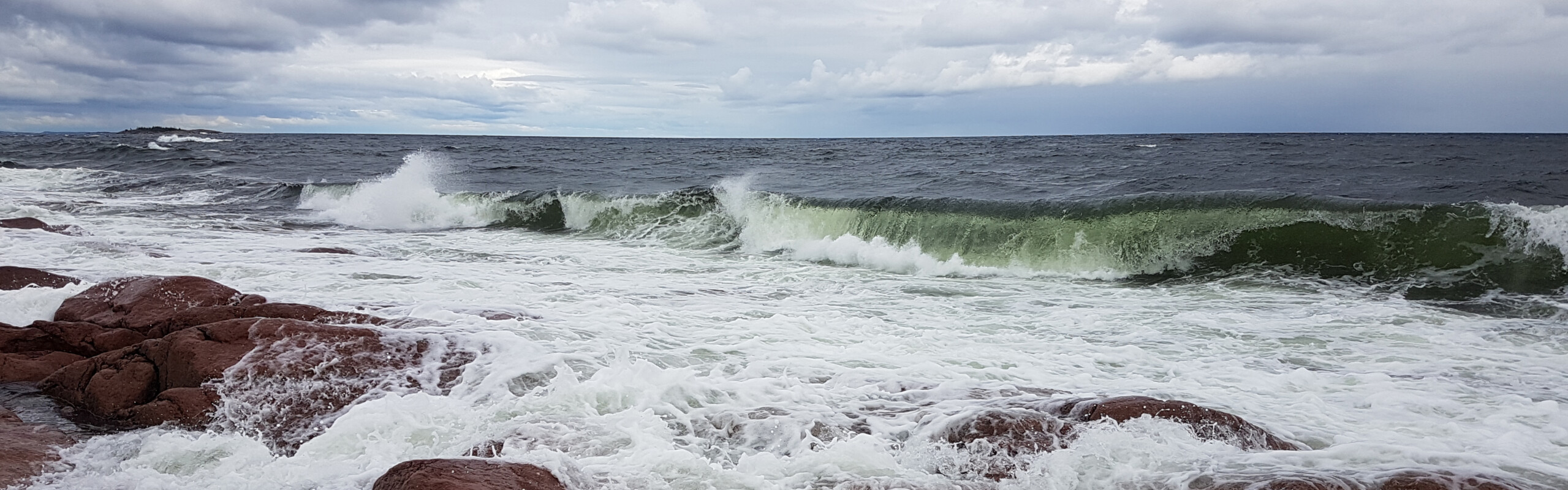 vågor slår mot röda klippor och en dramatisk himmel