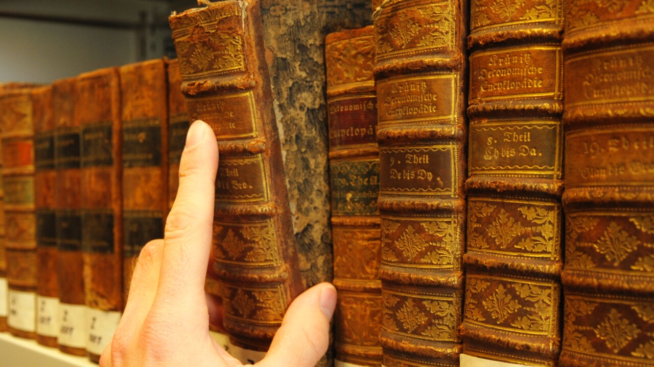 Hand som drar ut en gammal bok från en bibliotekshylla.