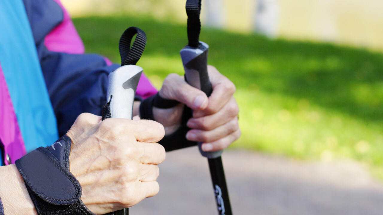 Närbild på händer som håller i stavar på en äldre person som tränar stavgång.