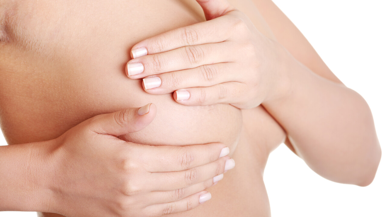 Kvinna som känner igenom sina bröst för att upptäcka eventuell cancerknöl.