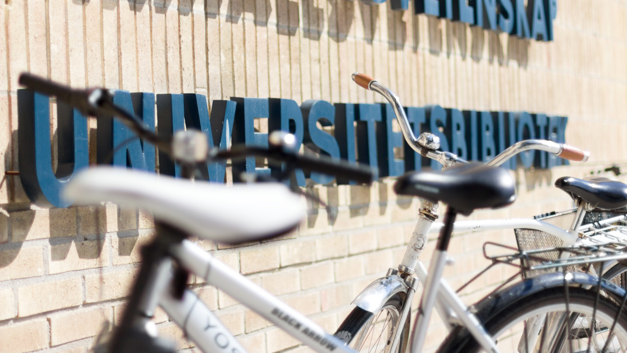 Universitetsbibliotekets fasad med skylt och cyklar i förgrunden.