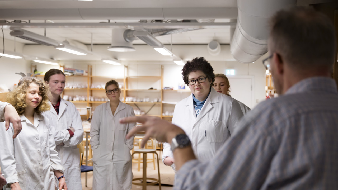 Pepole in lab coats listening to a male professor