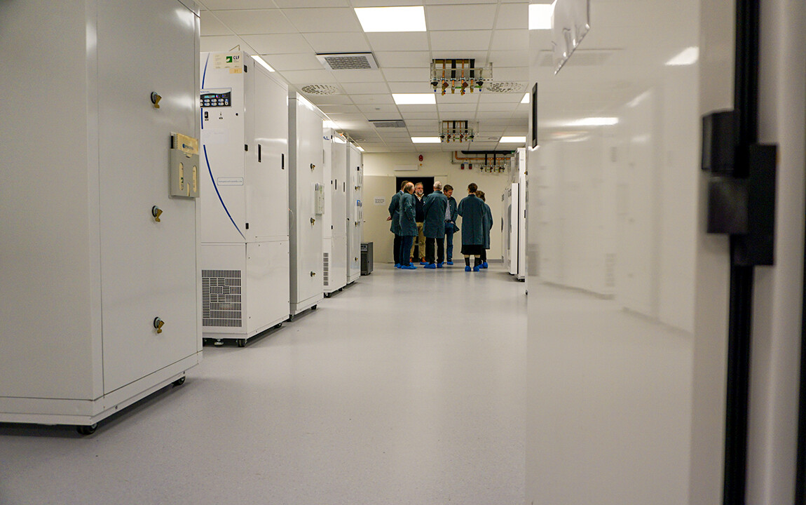 Korridor med vita odlingsskåp på båda sidor och en grupp av människor i gröna labbrock i slutet av korridoren