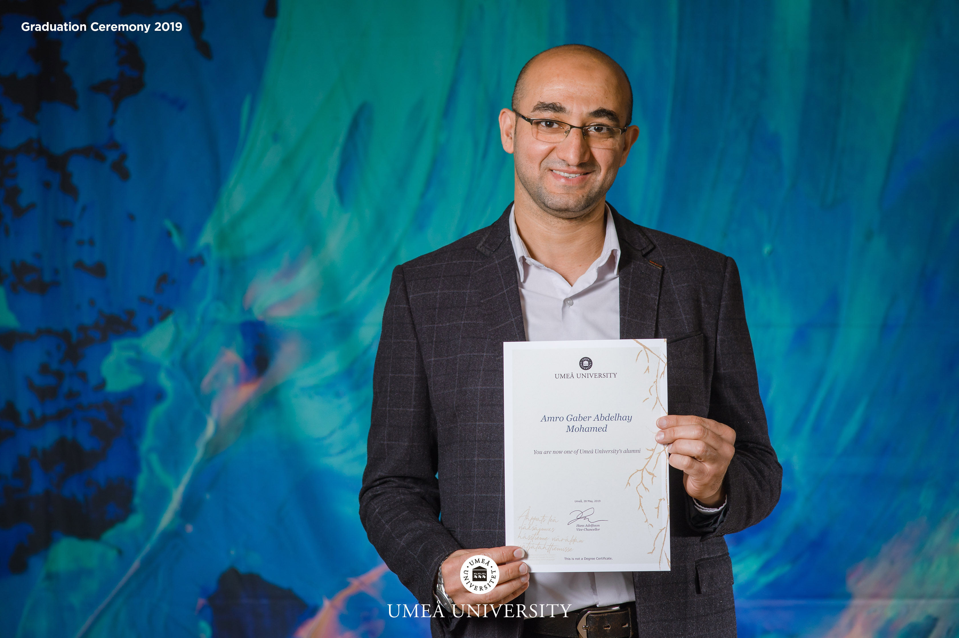 Student med diplom framför backdrop med norrskensmotiv