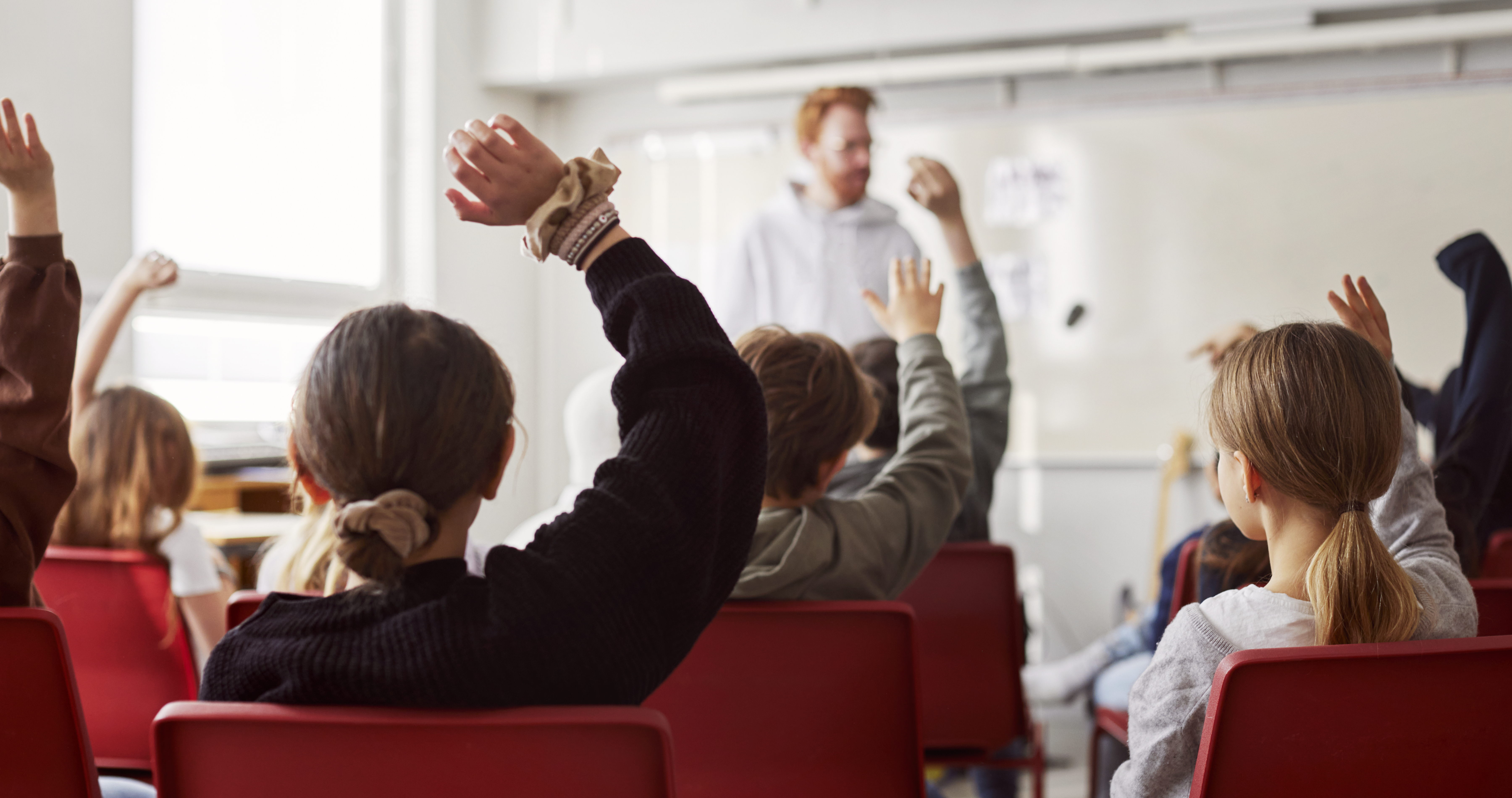Barn i klassrum räcker upp handen.
