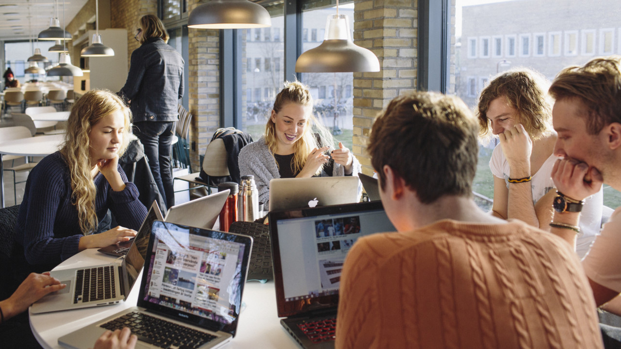 Flera studenter med bärbara datorer pluggar tillsammans vid ett runt bord i kafeterian i Humanisthuset på Umeå universitet