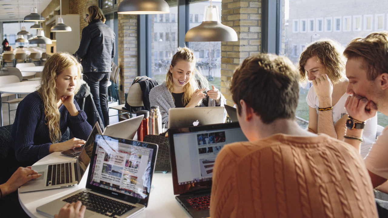 A group pf students around a table studying with their laptops in front of them