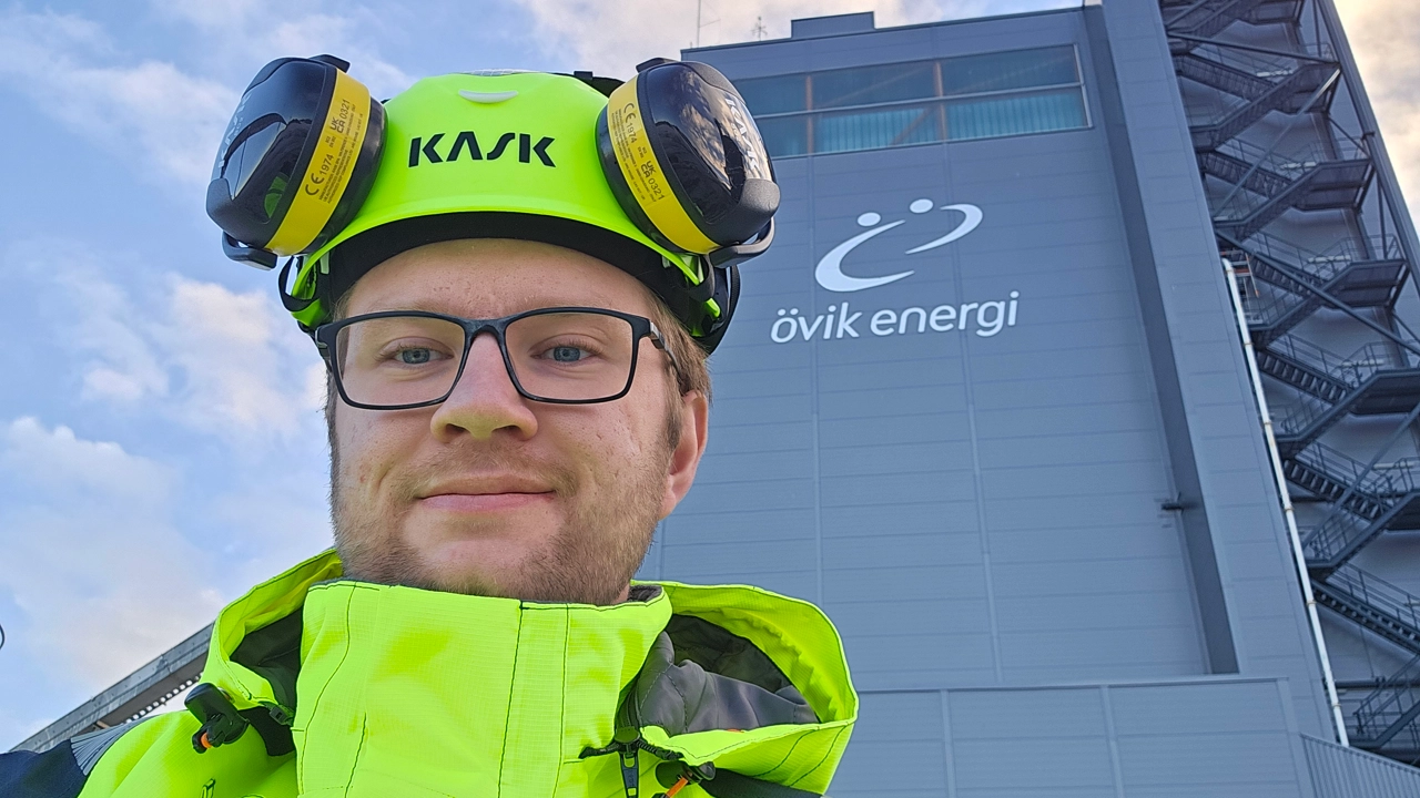 Porträttbild på Axel Lindberg med skyddshjälm och reflexkläder, i bakgrunden kraftvärmeverket i Övik