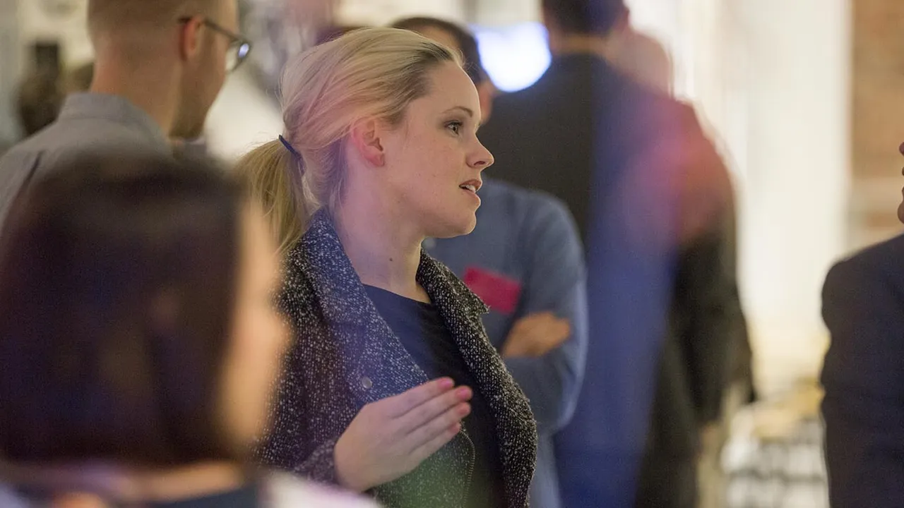 Focus is on a woman, standing i a crowd, mingling