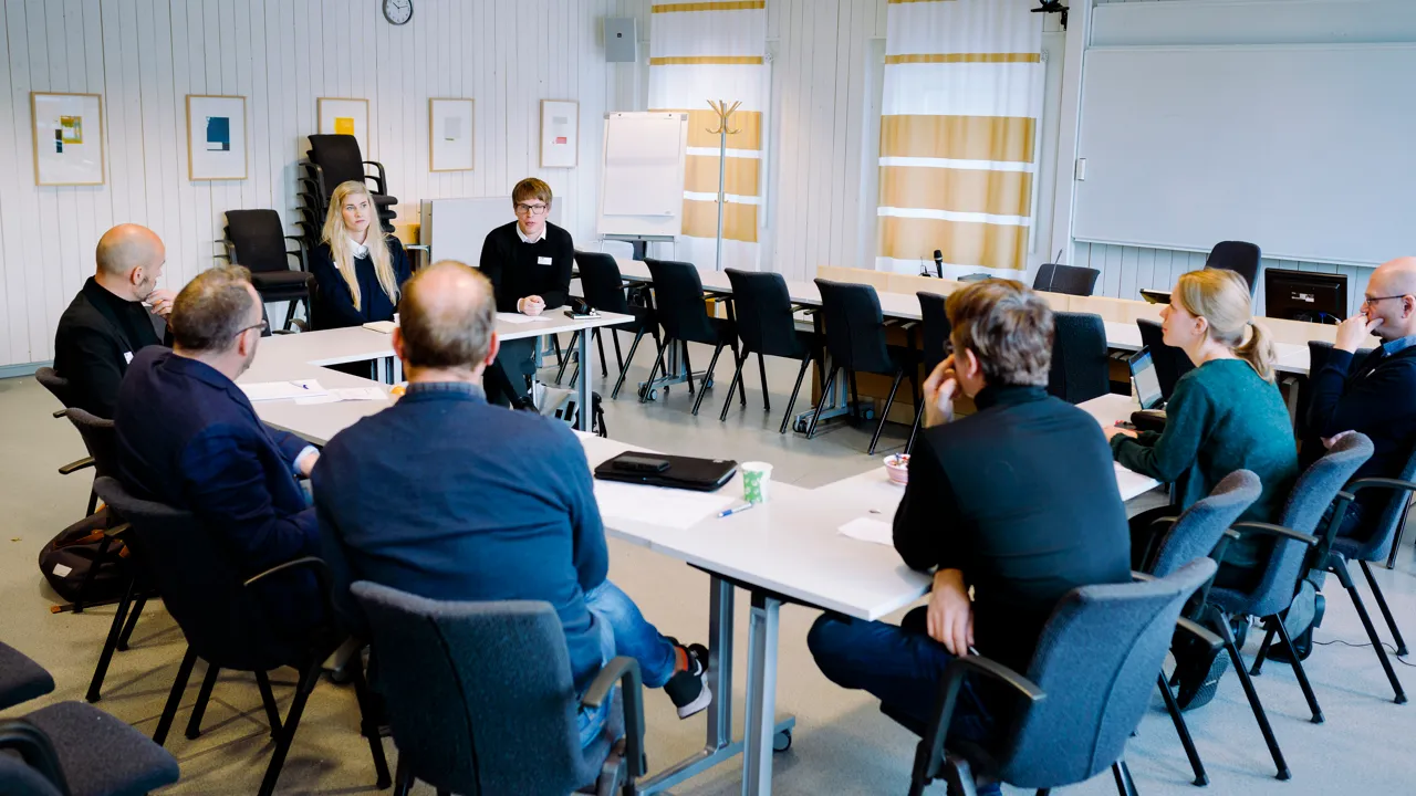 Eight people sat at a table formation facing each other in a conference room.