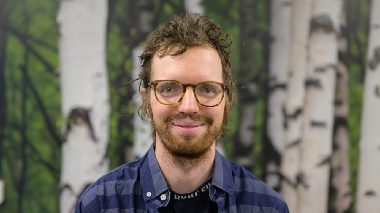 A man with a beard standing in front of a birch forest wallpaper background