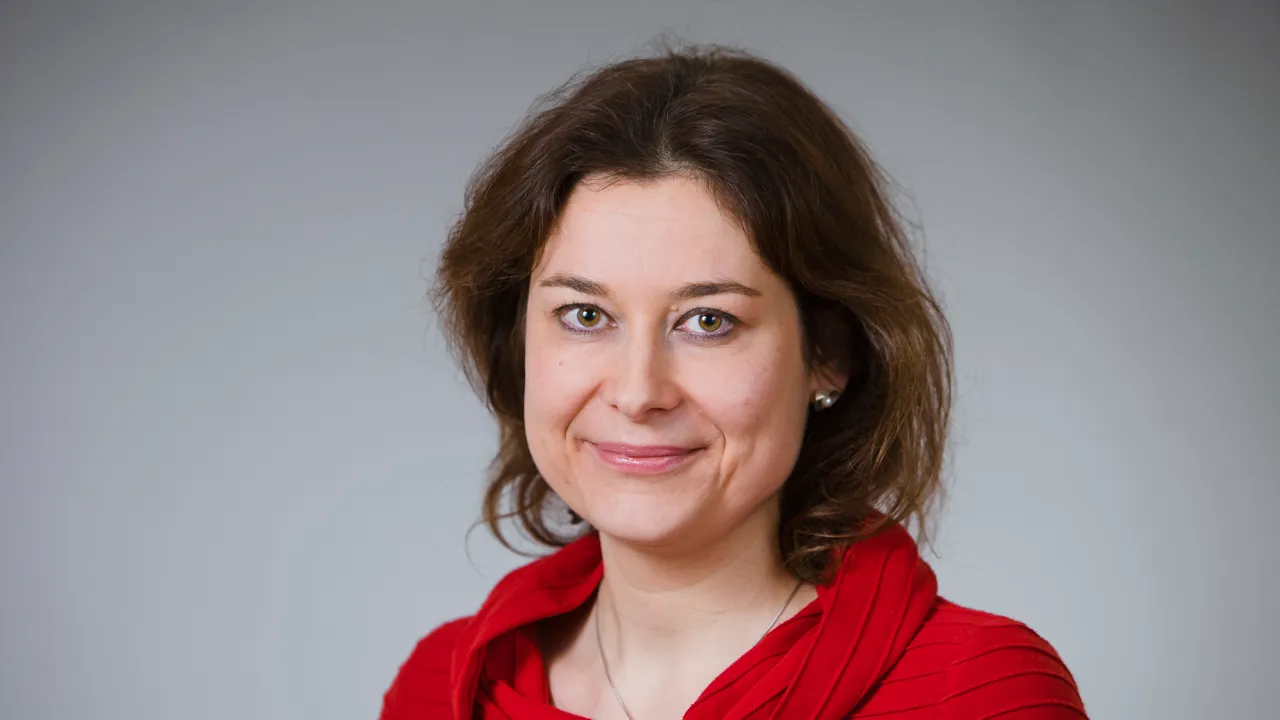 Porträttbild på en kvinna med röd tröka. Bakgrunden är blå.