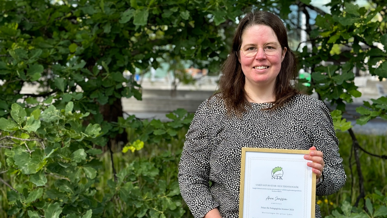 Kvinna håller i ett diplom och tittar in i kameran.