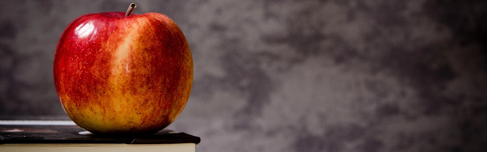 Ett rött äpple som ligger på en trave böcker.